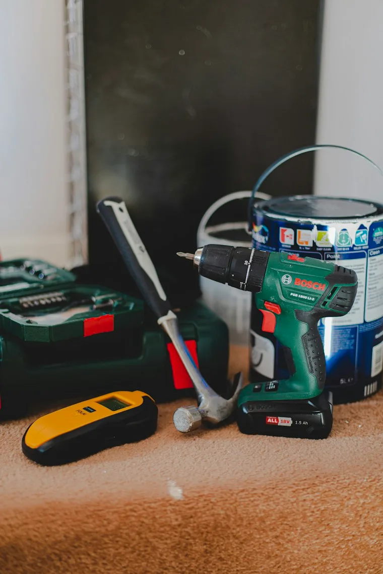 Cordless drill, hammer and stud finder laid out for a home repair job
