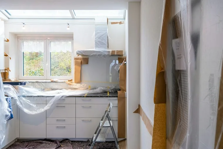 Kitchen under renovation with cabinets covered in protective paper and plastic