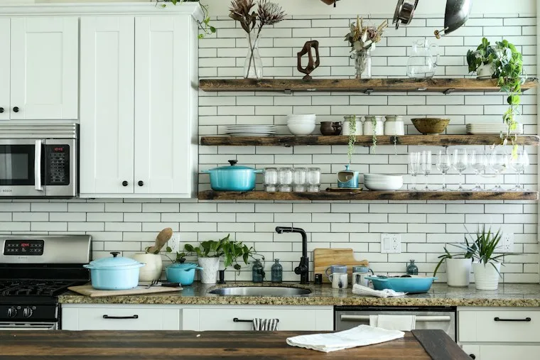 Kitchen with white cabinets, subway tile and open wood shelves holding cookware