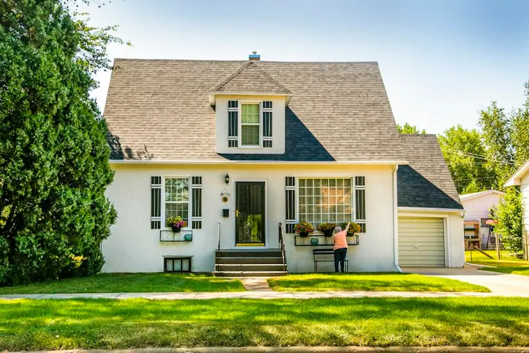 White single-family house with a green lawn and mature trees on a sunny day
